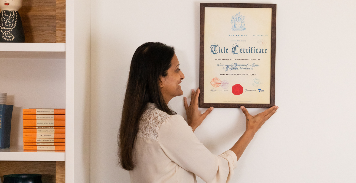 Landscape (1.911) Recommended size 1200 x 628 (1) Woman smiling while hanging Commemorative Title on her wall as her frequently asked questions have been answered