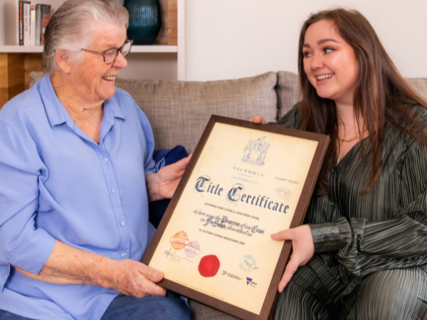 Woman is handing her happy grandmother a Commemorative Title after purchasing from the shopping cart.